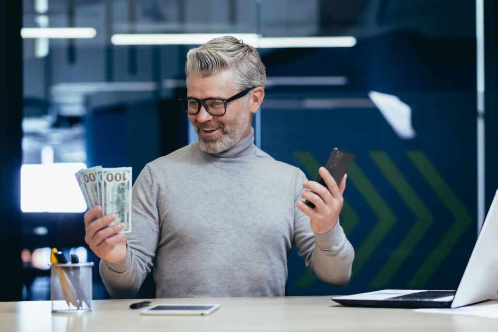 Homem Segurando Dinheiro E Celular, Usando O Programa E Indicação Da Upbet.