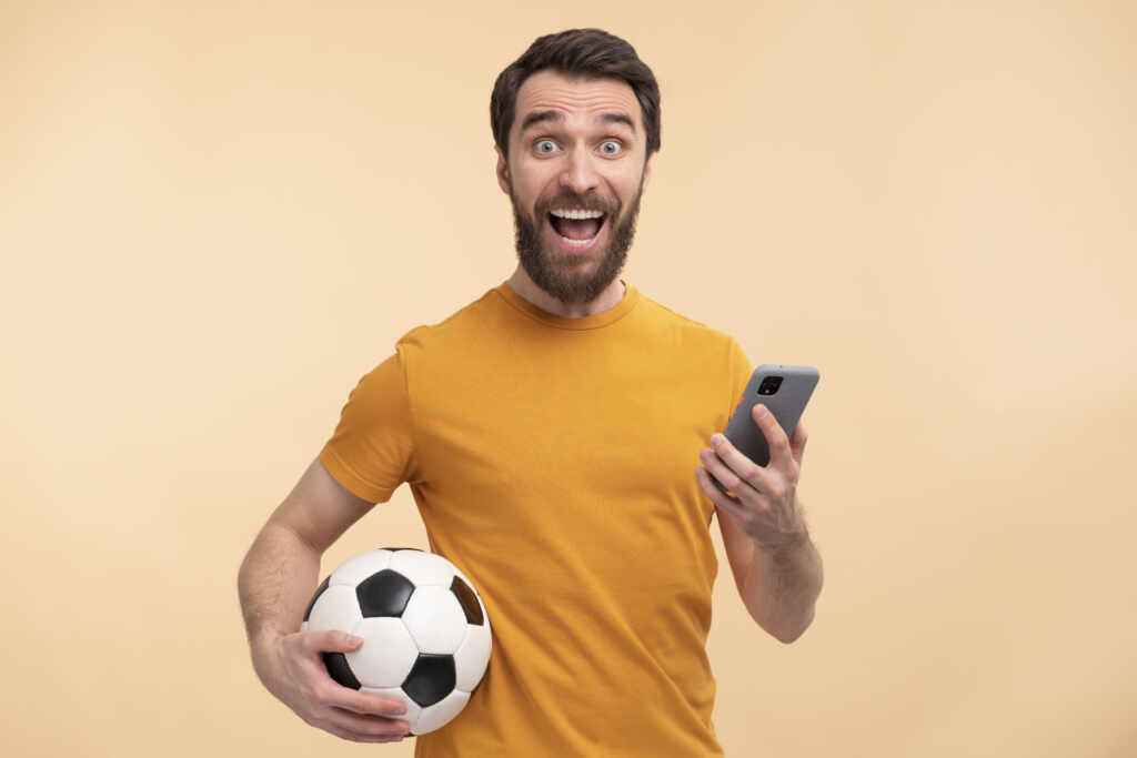 BetFusion: personalização que converte visita em experiência retrato de um jovem animado olhando para seu smartphone e segurando uma bola